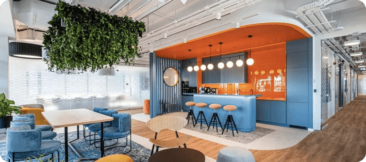 Modern coworking lounge with vibrant blue counter, orange accents, and collaborative workspace seating